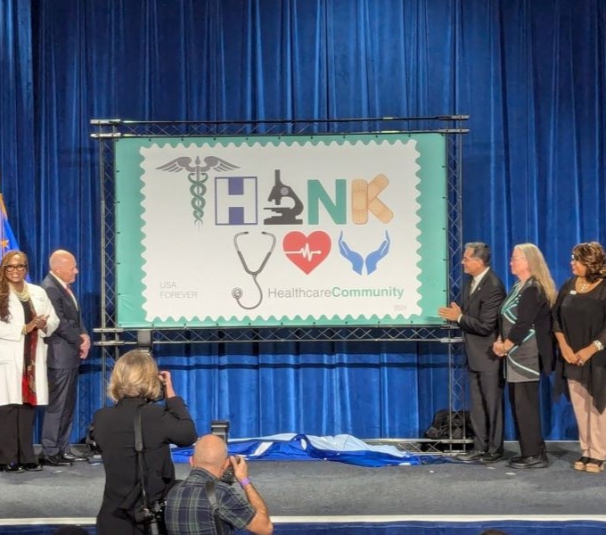 The new Forever stamp design displayed on a large screen with event attendees on a stage.