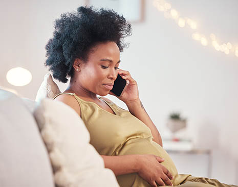A pregnant woman rests her hand on her abdomen while talking on a cell phone. 