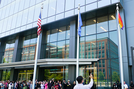Onlookers view the raised Pride flag alongside the American flag outside of HRSA's office in Rockville, MD.