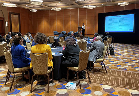 HRSA Acting Regional Administrator Aphrodyi Antoine speaking in front of a conference room with attendees at the Western Healthcare Forum in Seattle, Washington.