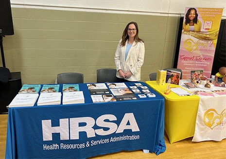HRSA staff member stands at the HRSA event display table