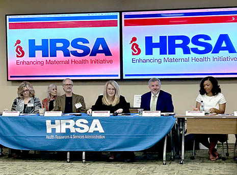 HRSA Administrator Johnson, MCHB Associate Administrator Dr. Warren and others seated at a table at the front of a meeting room.