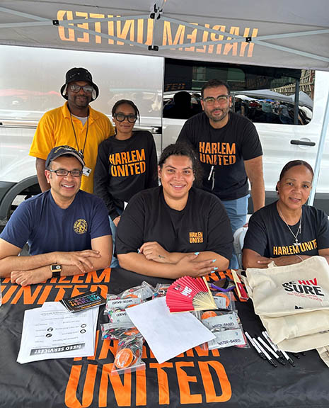 Group portrait of HRSA’s Chandak Ghosh and Octavia Wisseh with others seated at an exhibit booth at the New York City National HIV Testing Day event.
