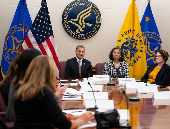 HHS Secretary Xavier Becerra and others are seated at a conference table.