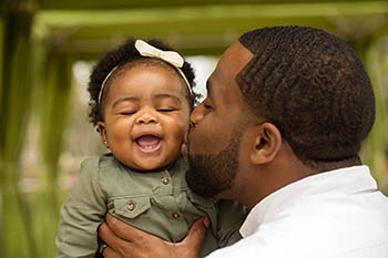 An adult male kisses the cheek of an infant girl.