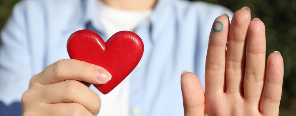 A woman holding a heart-shaped object in one hand and showing a blue circle symbol written on the finger of her other hand. 