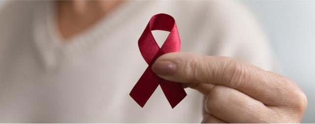 A person is holding a red ribbon that represents HIV awareness.