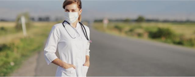 A health professional is standing on a rural road while wearing a mask.